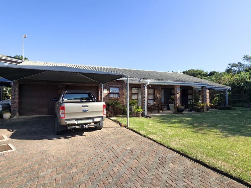 Front view of a single-story brick house featuring a paved driveway, carport, covered patio area, and a well-maintained lawn.