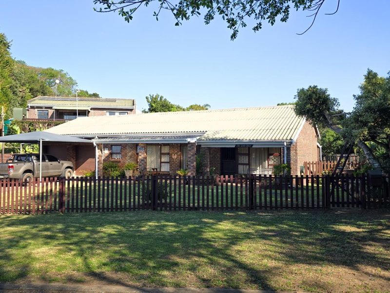 Front view of a single-story brick house featuring a corrugated metal roof, a carport, and a fenced front garden area.