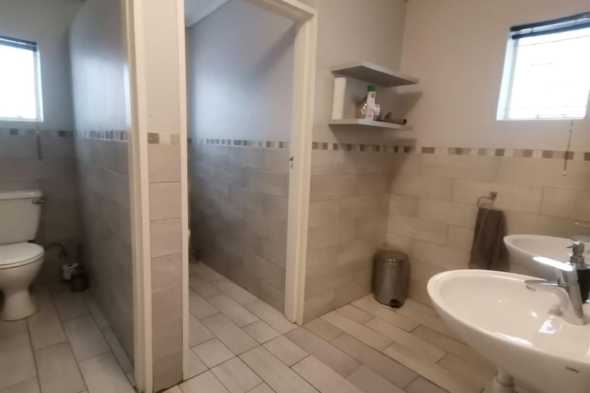 A functional office restroom featuring tiled walls, dual pedestal basins, and separate toilet cubicles with neutral finishes.