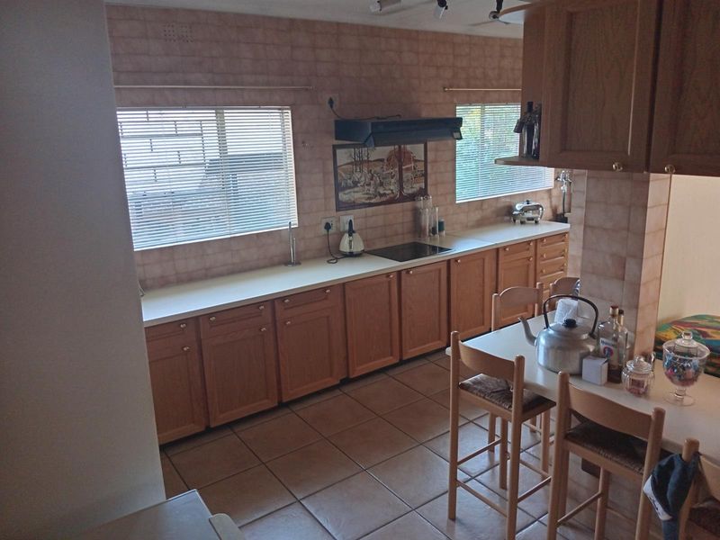 A functional kitchen featuring wooden cabinetry, laminate countertops, an electric hob with extractor fan, and tiled finishes throughout.
