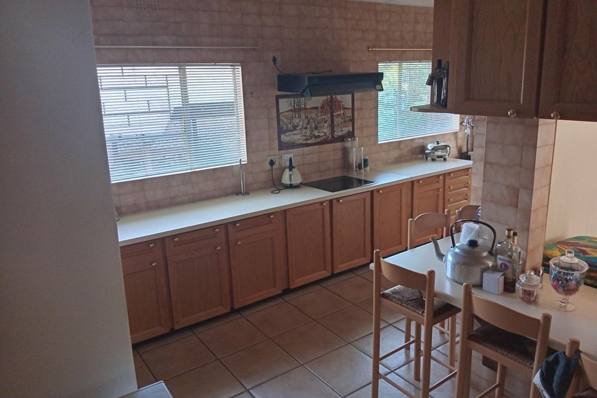 A functional kitchen featuring wooden cabinetry, laminate countertops, an electric hob with extractor fan, and tiled finishes throughout.