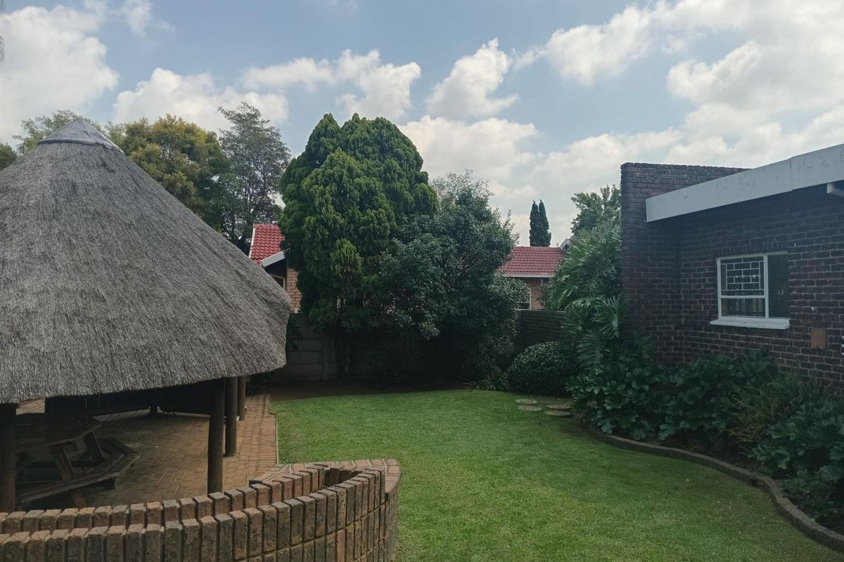 A private rear garden featuring a traditional thatch lapa, brick paved patio area, and established lawn with brick boundary walls.