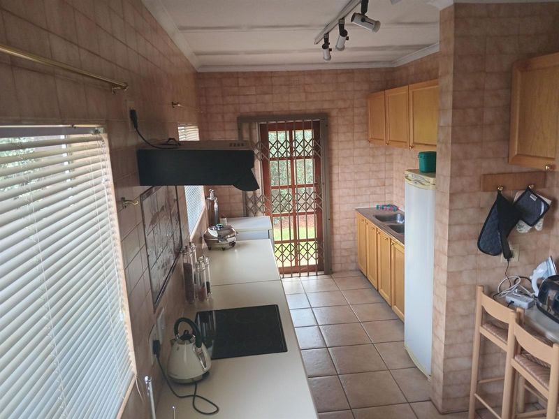 A functional kitchen featuring built-in cabinetry, laminate countertops, an electric hob, and tiled finishes throughout, with direct access to the exterior via a security gate.