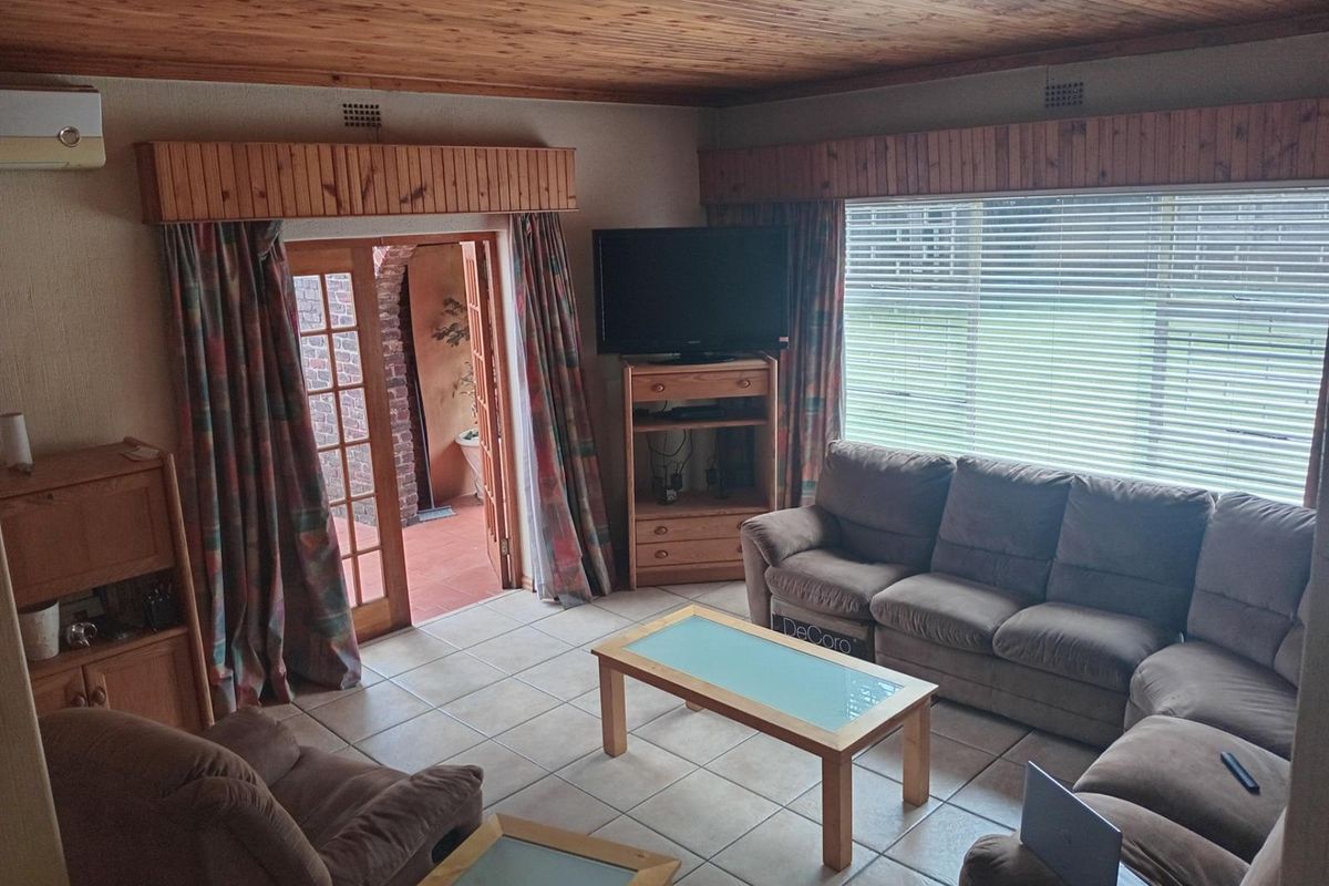 A living room featuring tiled flooring, a timber-paneled ceiling, and direct access to an outdoor patio area through timber-framed glass doors.