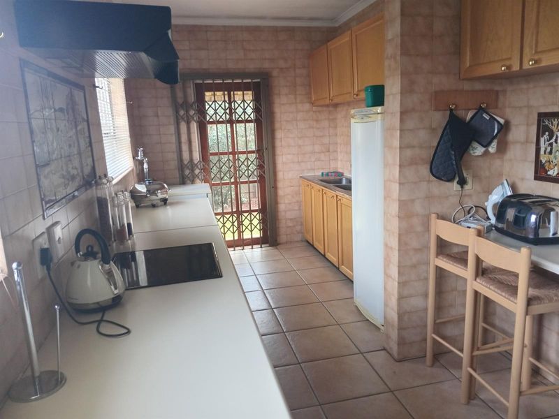 A functional kitchen featuring built-in wooden cabinetry, ceramic tile flooring, wall tiling, and an integrated hob with an extractor fan.