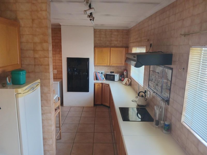 A functional kitchen featuring built-in wooden cabinetry, ceramic tile wall finishes, an electric hob with extractor fan, and tiled flooring.