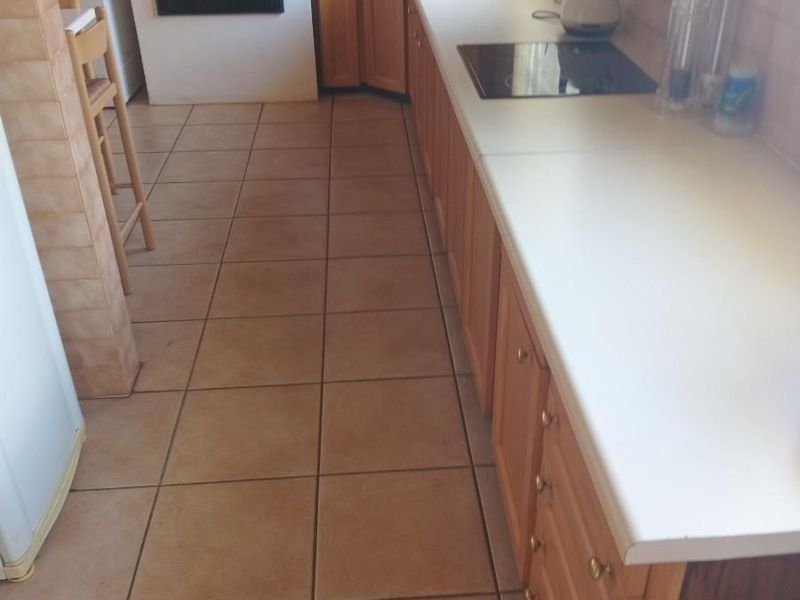 A functional kitchen featuring wooden cabinetry, laminate countertops, and ceramic tiled flooring with a built-in oven and electric hob.