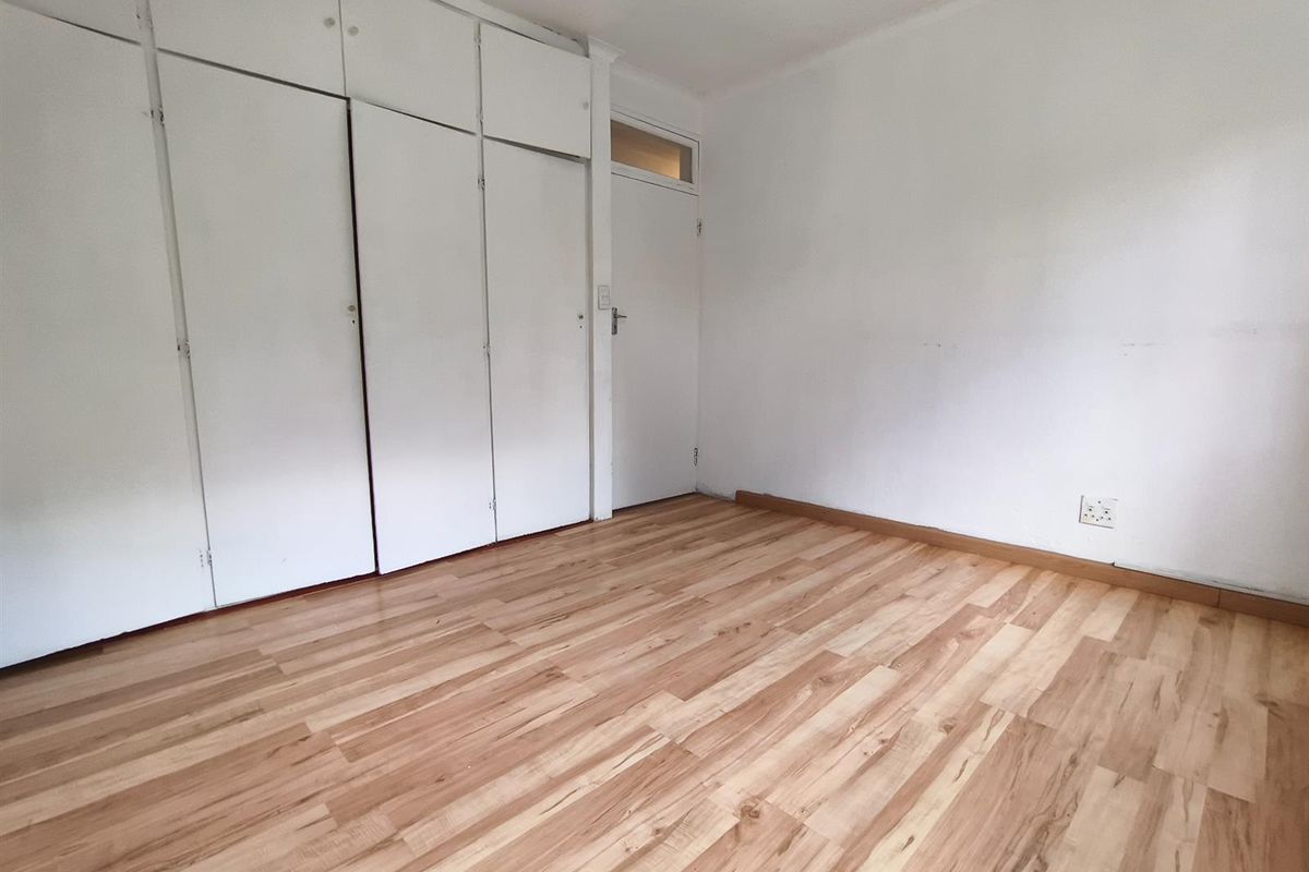 An empty bedroom featuring light-toned laminate flooring and extensive built-in cupboard storage with a neutral white finish.