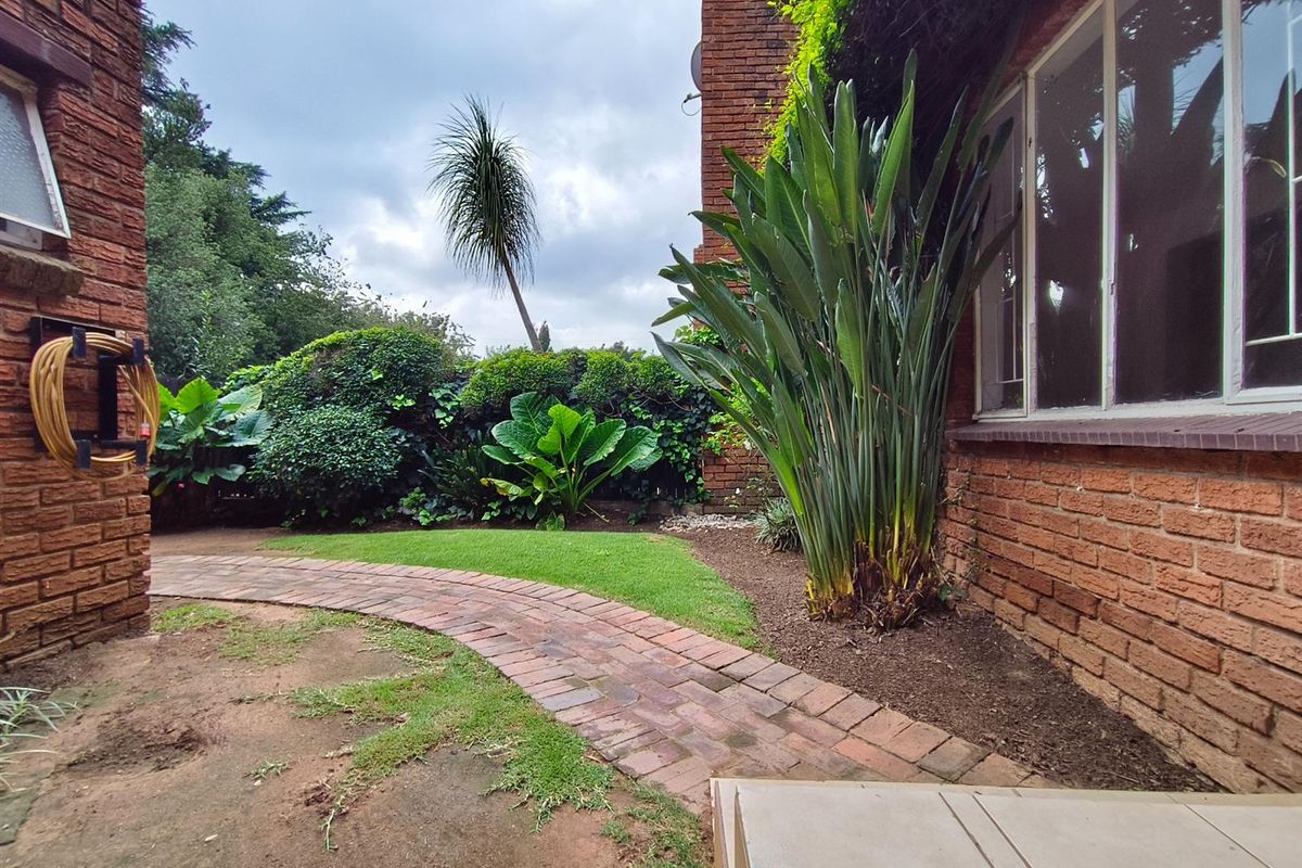 A rear garden area featuring a brick pathway, established landscaping, and a brick townhouse facade.