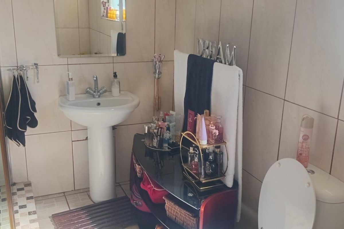 A functional bathroom featuring a pedestal washbasin, a shower enclosure with tiled finishes, and a standard toilet, finished with neutral wall and floor tiles.