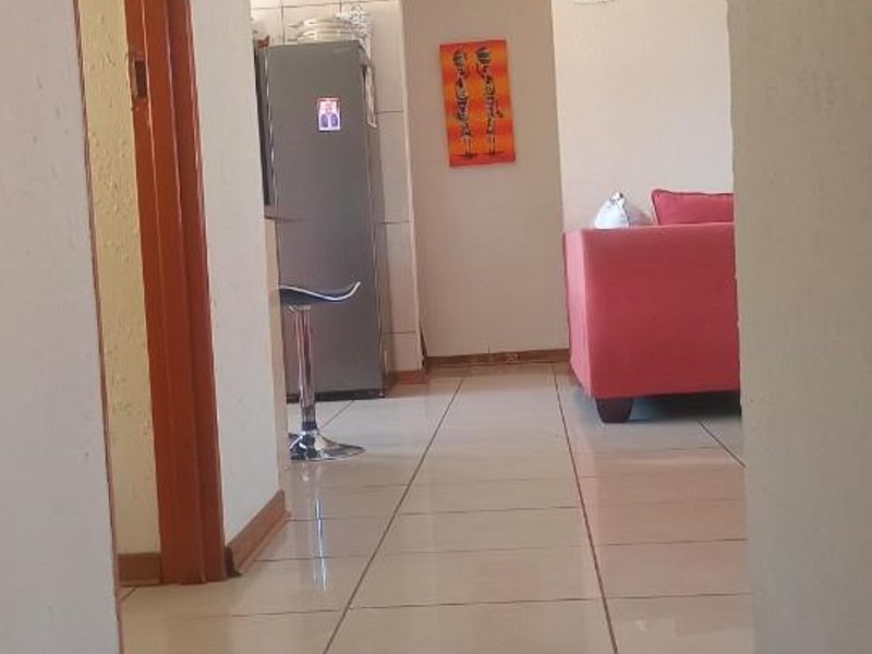 A view from a hallway looking into an open plan living and kitchen area featuring tiled flooring throughout.