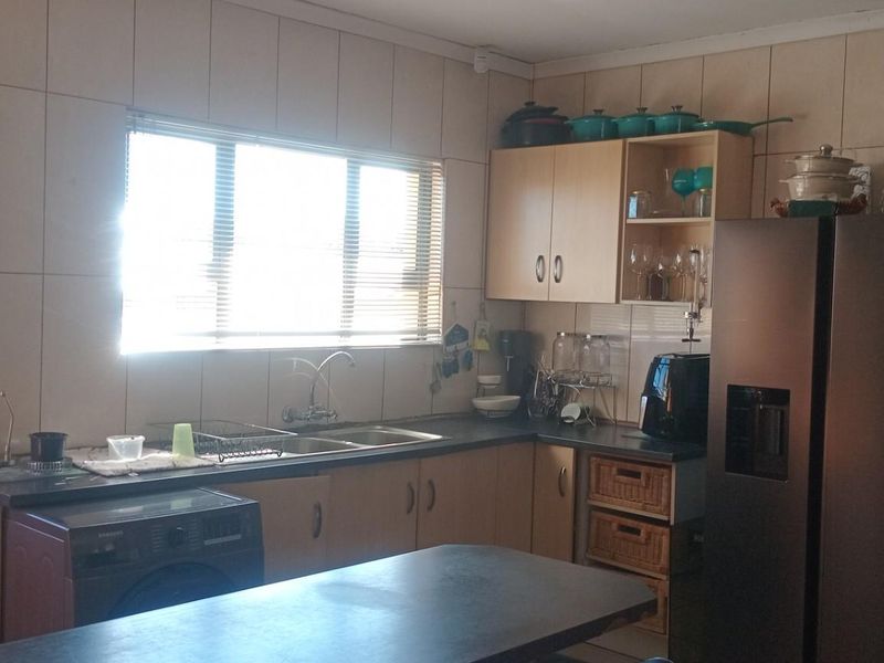 A functional kitchen featuring built-in cabinetry, laminate countertops, a double sink, and tiled splashbacks, offering a practical layout for daily meal preparation.