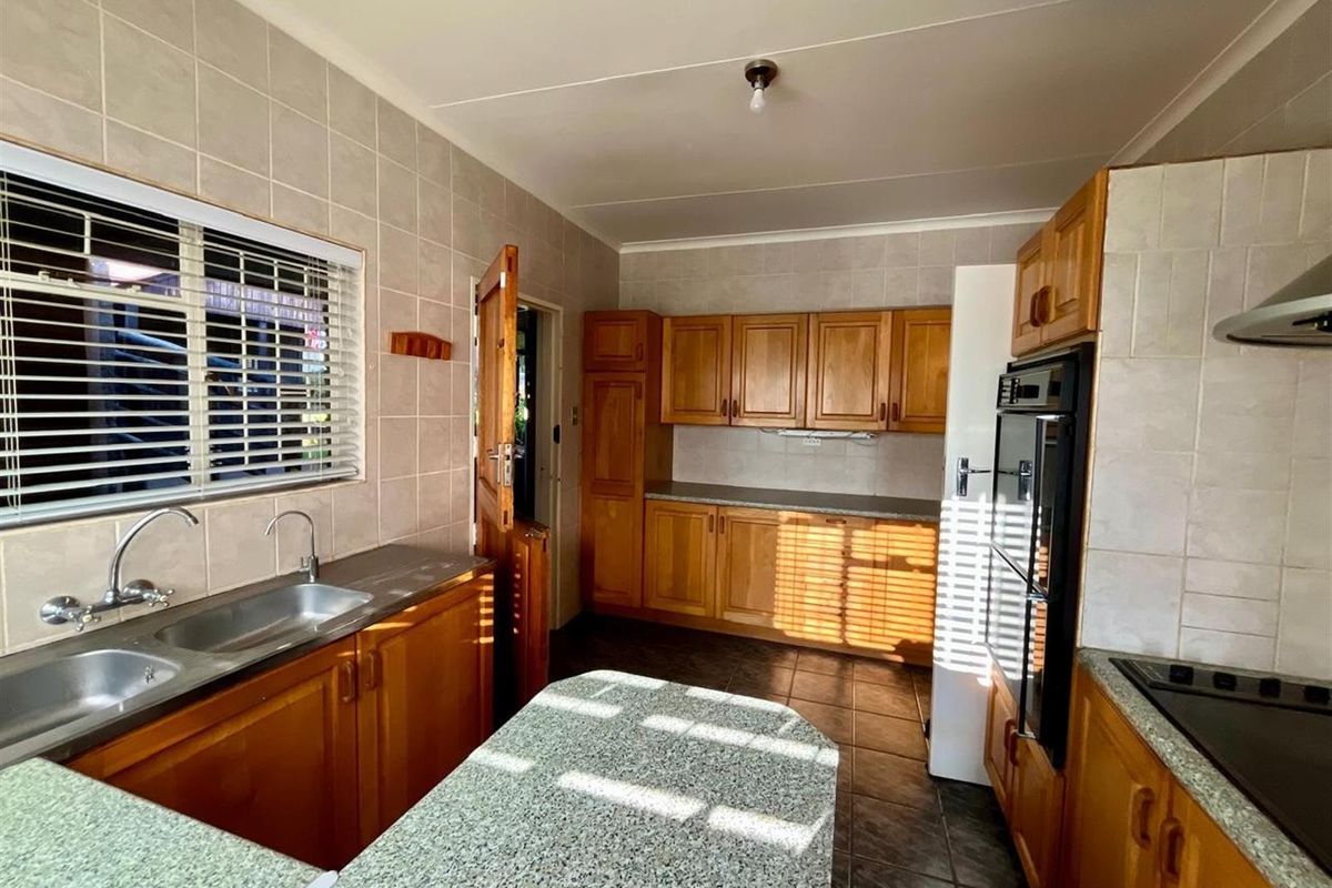 A functional kitchen featuring wooden cabinetry, laminate countertops, a double stainless steel sink, built-in oven, and tiled finishes throughout.