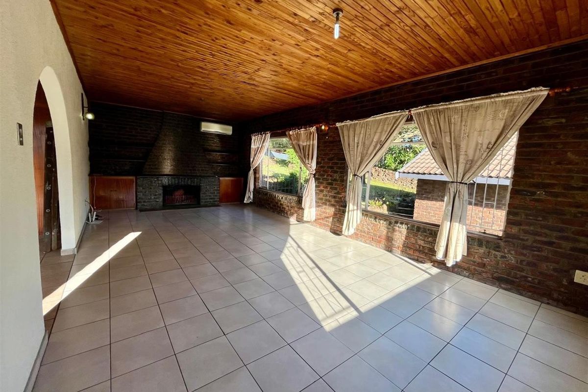 Spacious living area featuring exposed brick walls, a timber ceiling, tiled floors, and a built-in fireplace, offering a warm and versatile space.
