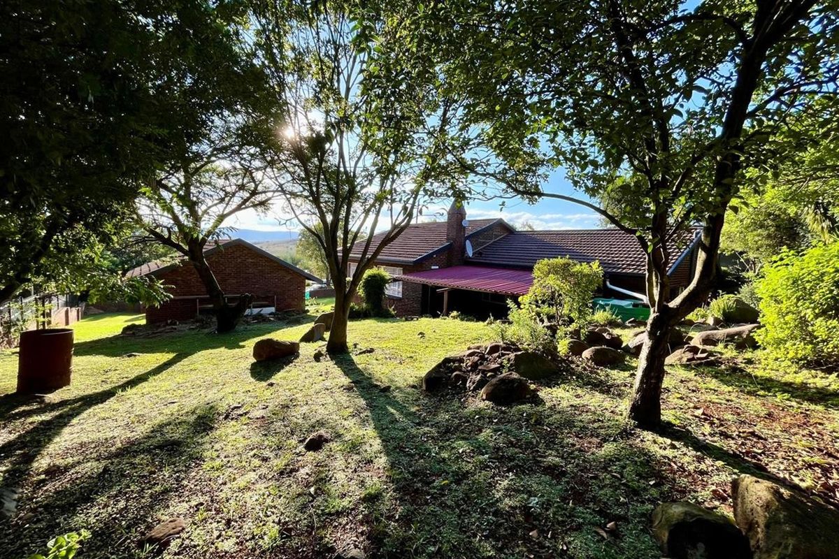 Rear view of the brick house featuring a covered patio area, tiled roof, and established garden surroundings.