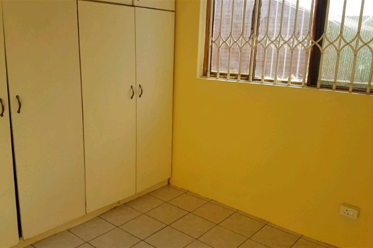 A bedroom featuring built-in cupboards, tiled flooring, and a window fitted with security bars.