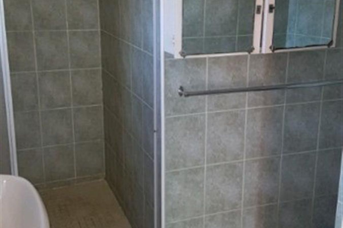 A compact bathroom featuring a shower enclosure, toilet, and wall-mounted medicine cabinet with dated green wall tiles and neutral floor tiling.
