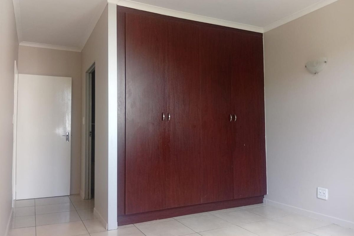 A clean, empty bedroom featuring dark wood built-in cupboards, neutral wall paint, and light-colored floor tiles.
