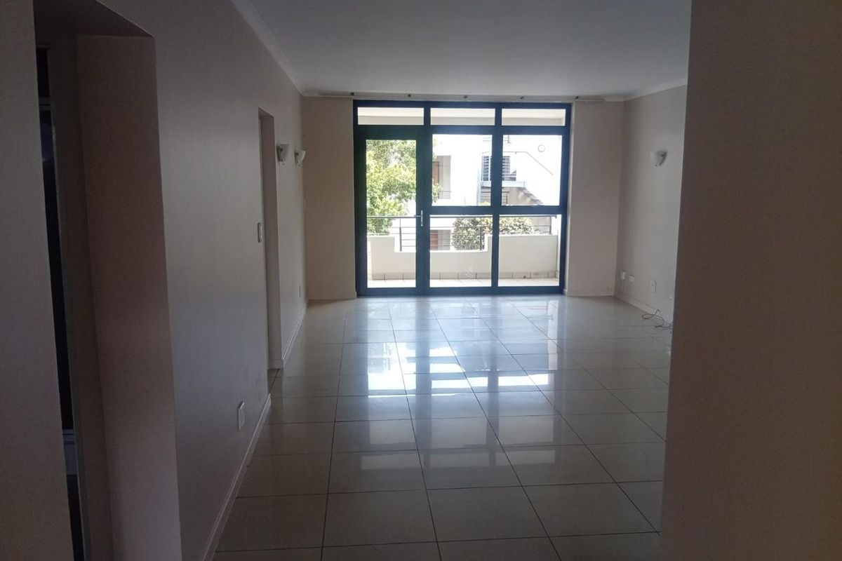 A bright, empty living area featuring polished tiled flooring and a large sliding glass door leading to an outdoor balcony.