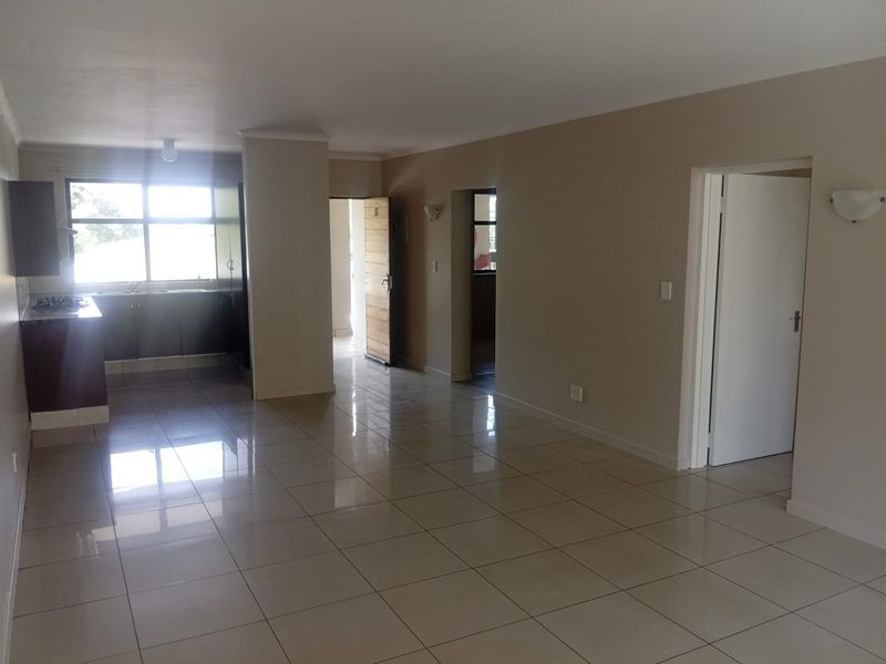 An open-plan living and kitchen area featuring neutral tiled flooring, built-in kitchen cabinetry, and direct access to adjacent rooms.
