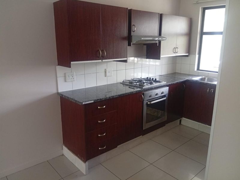 A functional kitchen featuring dark wood cabinetry, granite countertops, a gas hob, built-in oven, and tiled flooring in a clean, empty space.