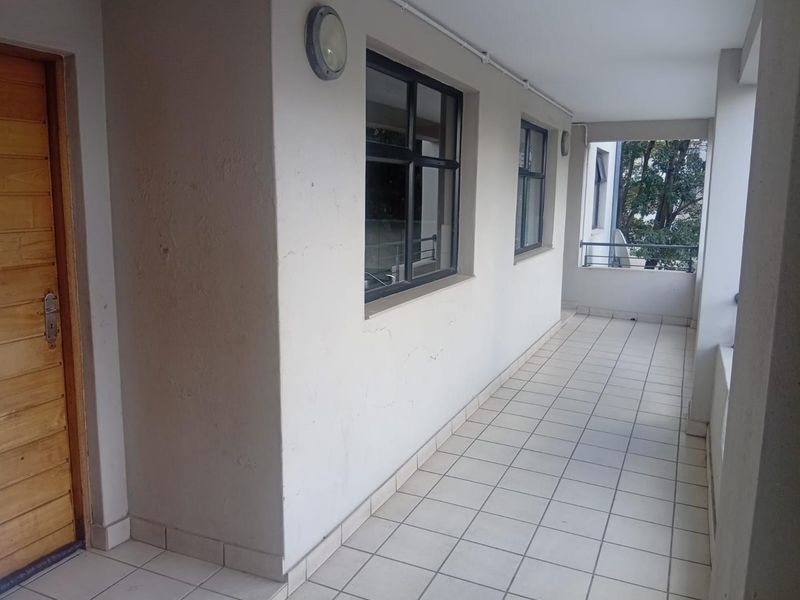 A covered balcony area featuring tiled flooring, a wooden entrance door, and metal balustrades, providing an outdoor transition space for the apartment.
