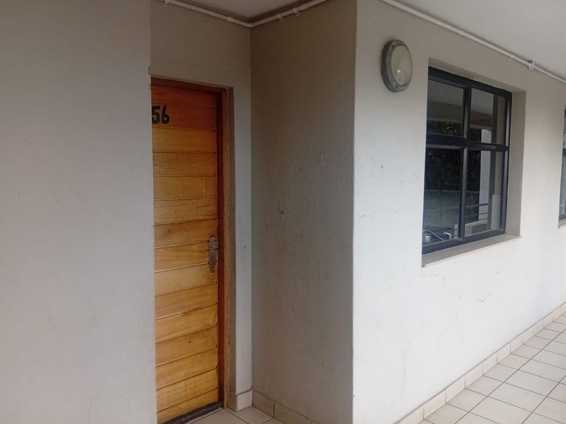 Exterior view of an apartment entrance featuring a timber door, tiled walkway, and external wall lighting.