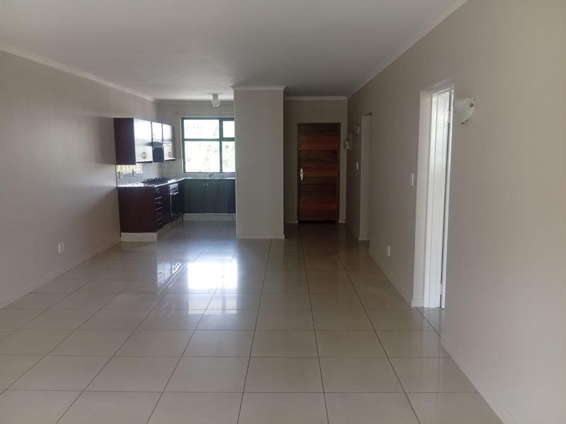 Spacious open-plan living area featuring neutral tiled flooring and a functional kitchen with built-in cabinetry, oven, and hob.