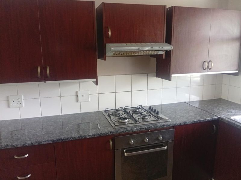 A functional kitchen featuring dark wood cabinetry, granite-look laminate countertops, a built-in oven, gas hob, and a tiled backsplash.