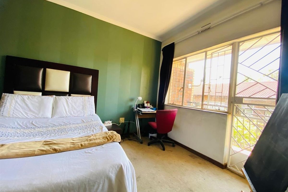 A bedroom featuring a large window with security bars and direct access to an outdoor area, finished with carpet flooring and an accent wall.