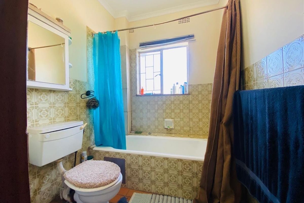 A dated bathroom featuring a built-in bathtub with shower, toilet, and vintage patterned wall tiles.