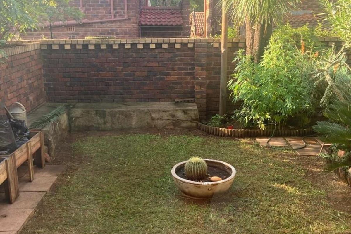 A private rear garden featuring a brick boundary wall, established greenery, and a small lawn area.
