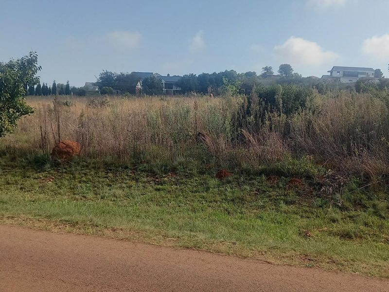 A view of a vacant residential plot featuring natural vegetation and grass, situated in a developed neighborhood setting.
