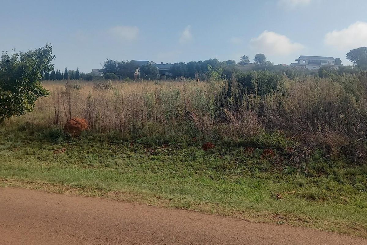 A view of a vacant residential plot featuring natural vegetation and grass, situated in a developed neighborhood setting.