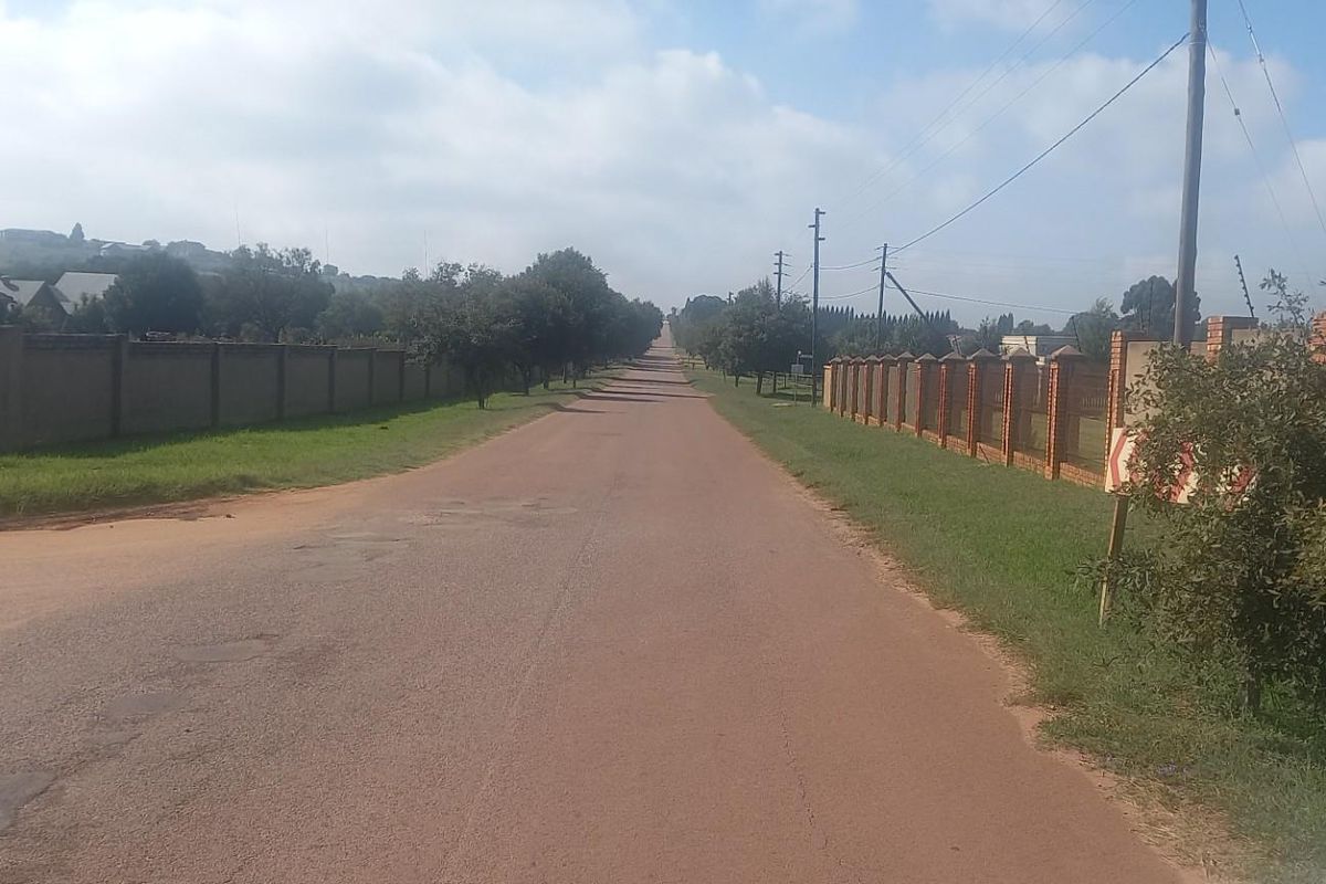 A view of the street approach showing the unpaved road, surrounding perimeter walls, and established residential neighborhood infrastructure.