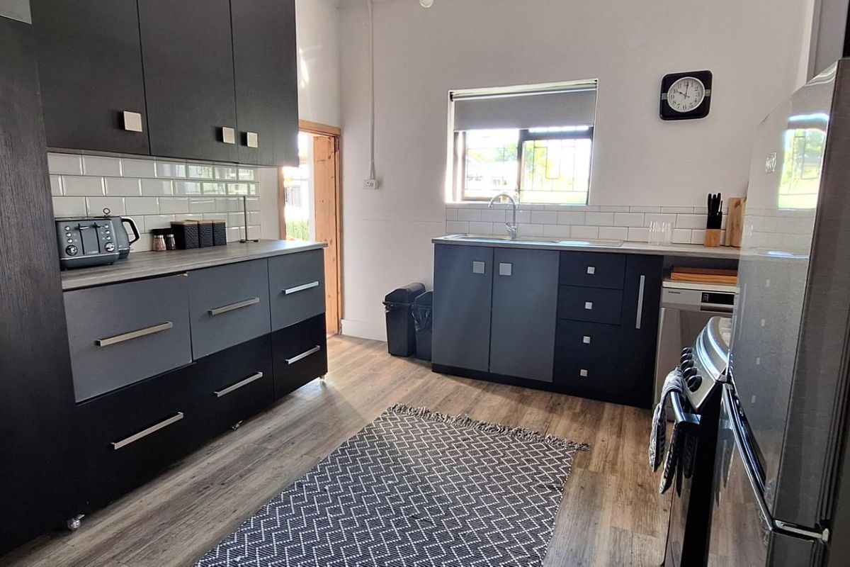 Modern kitchen featuring dark cabinetry, subway tile backsplash, stainless steel sink, and wood-look flooring with direct access to the exterior.