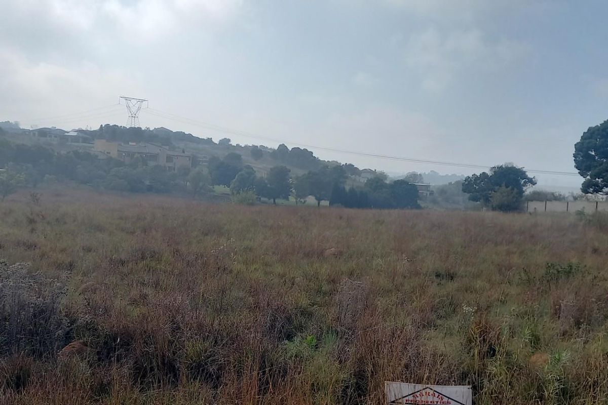 A view of a vacant residential plot featuring natural grass coverage and surrounding landscape.