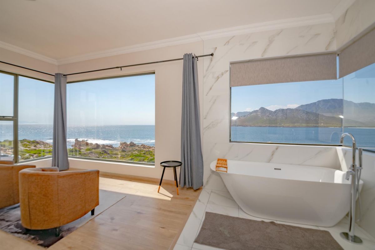 A luxurious bathroom featuring a freestanding bathtub, marble-look wall tiling, and expansive windows offering panoramic ocean and mountain views.