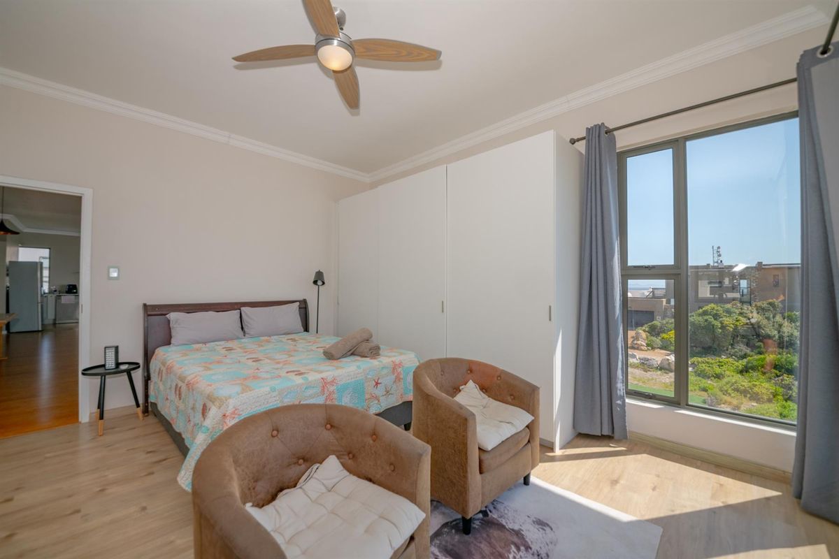 A bright bedroom featuring built-in wardrobes, a ceiling fan, and large windows offering natural light and scenic views.