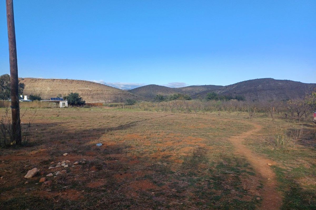 A wide-angle view of a vacant residential plot featuring natural terrain, sparse vegetation, and distant mountain views.