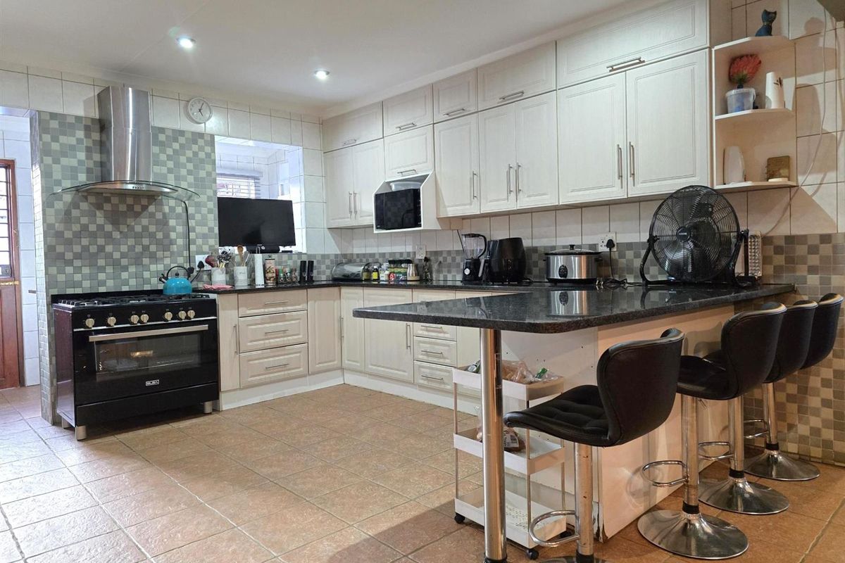 A functional kitchen featuring white cabinetry, dark granite countertops, a breakfast bar, and a black freestanding gas stove with a stainless steel extractor fan.