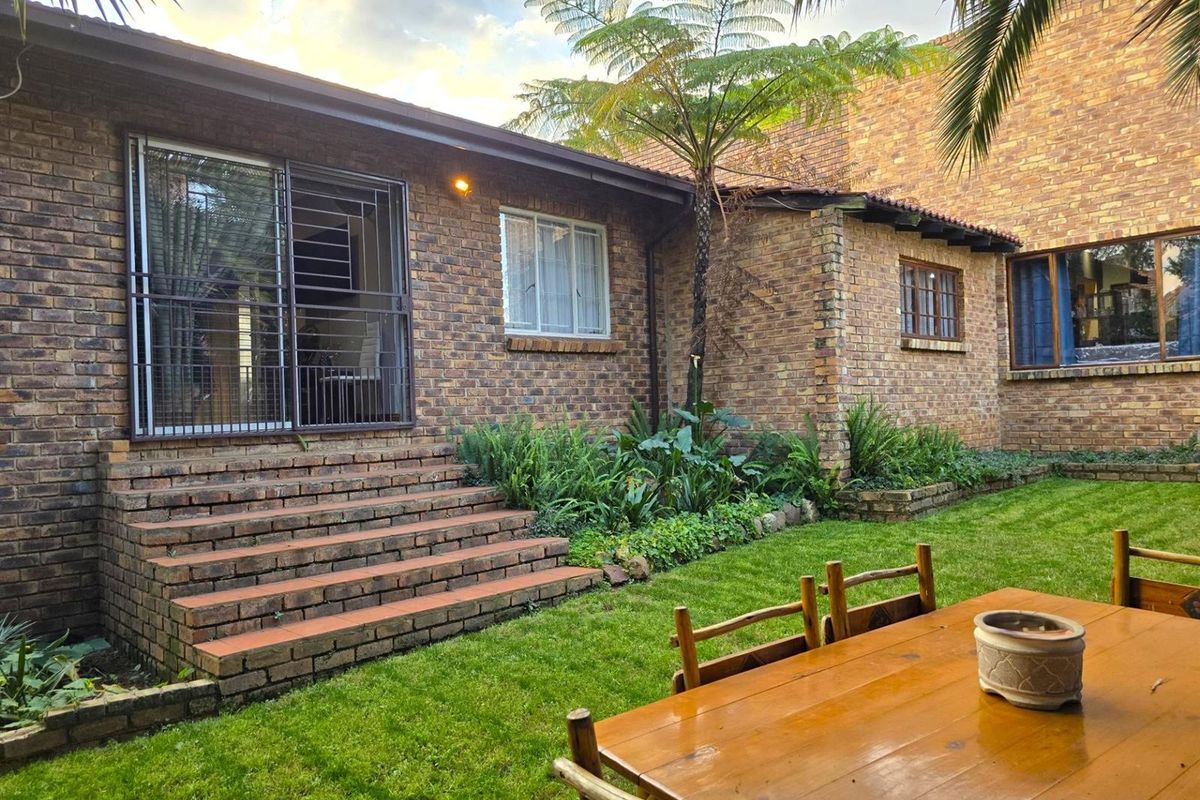 A well-maintained rear exterior view featuring face-brick facade, brick steps leading to a sliding door, and a landscaped garden area.