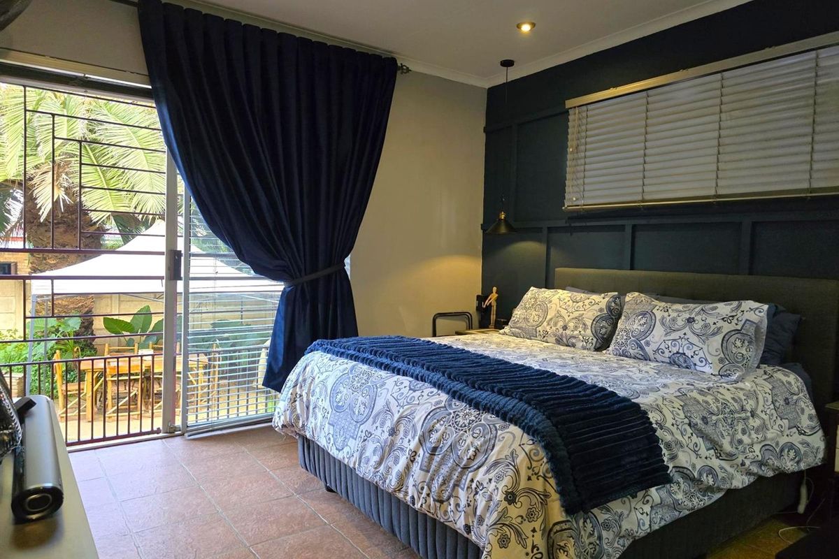 A well-maintained bedroom featuring dark accent wall paneling, tiled flooring, and a sliding glass door providing direct access to an outdoor patio area.