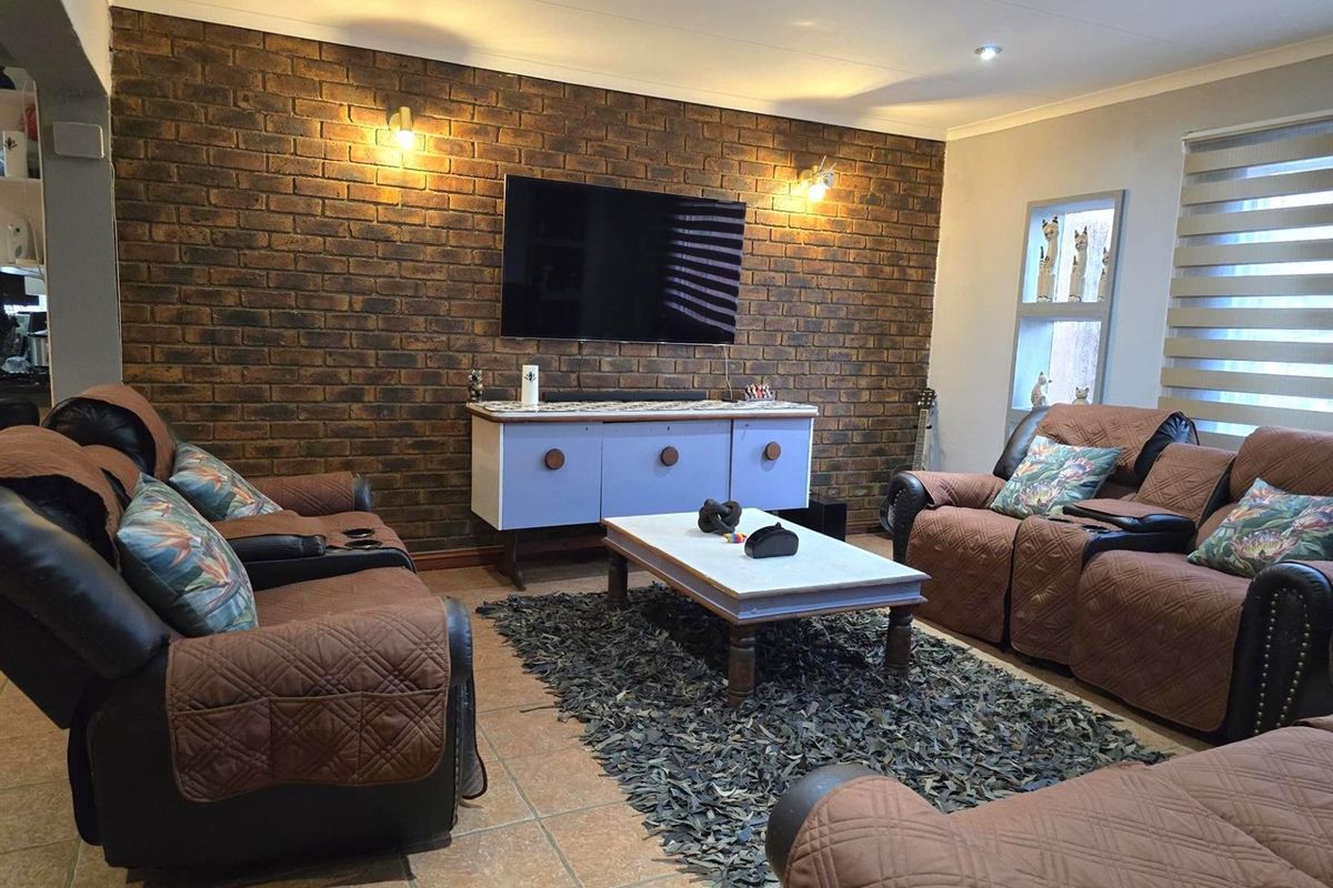 A cozy living room featuring a prominent exposed brick feature wall, tiled flooring, and recessed downlighting.