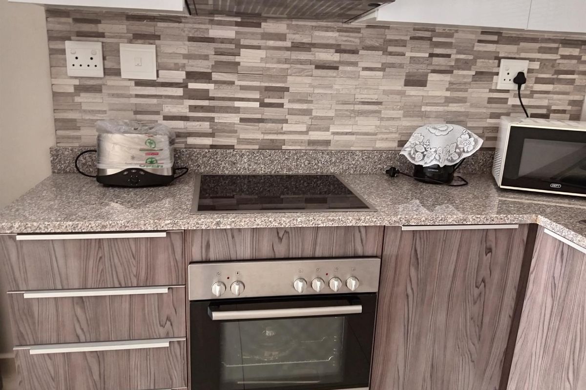 Modern kitchen featuring granite countertops, wood-grain cabinetry, a built-in Bosch oven, glass hob, and a stainless steel extractor fan.