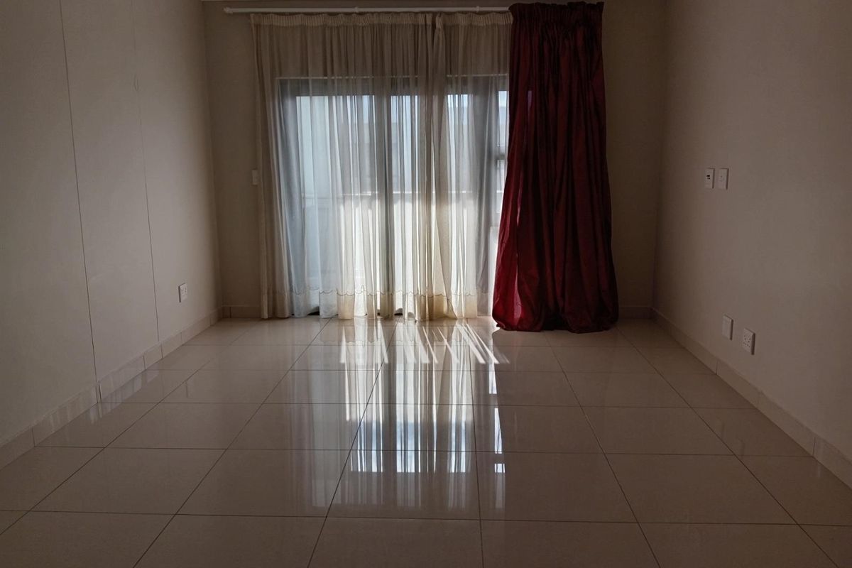 An empty living room featuring polished ceramic floor tiles, recessed ceiling lighting, and sliding glass doors leading to an outdoor area.