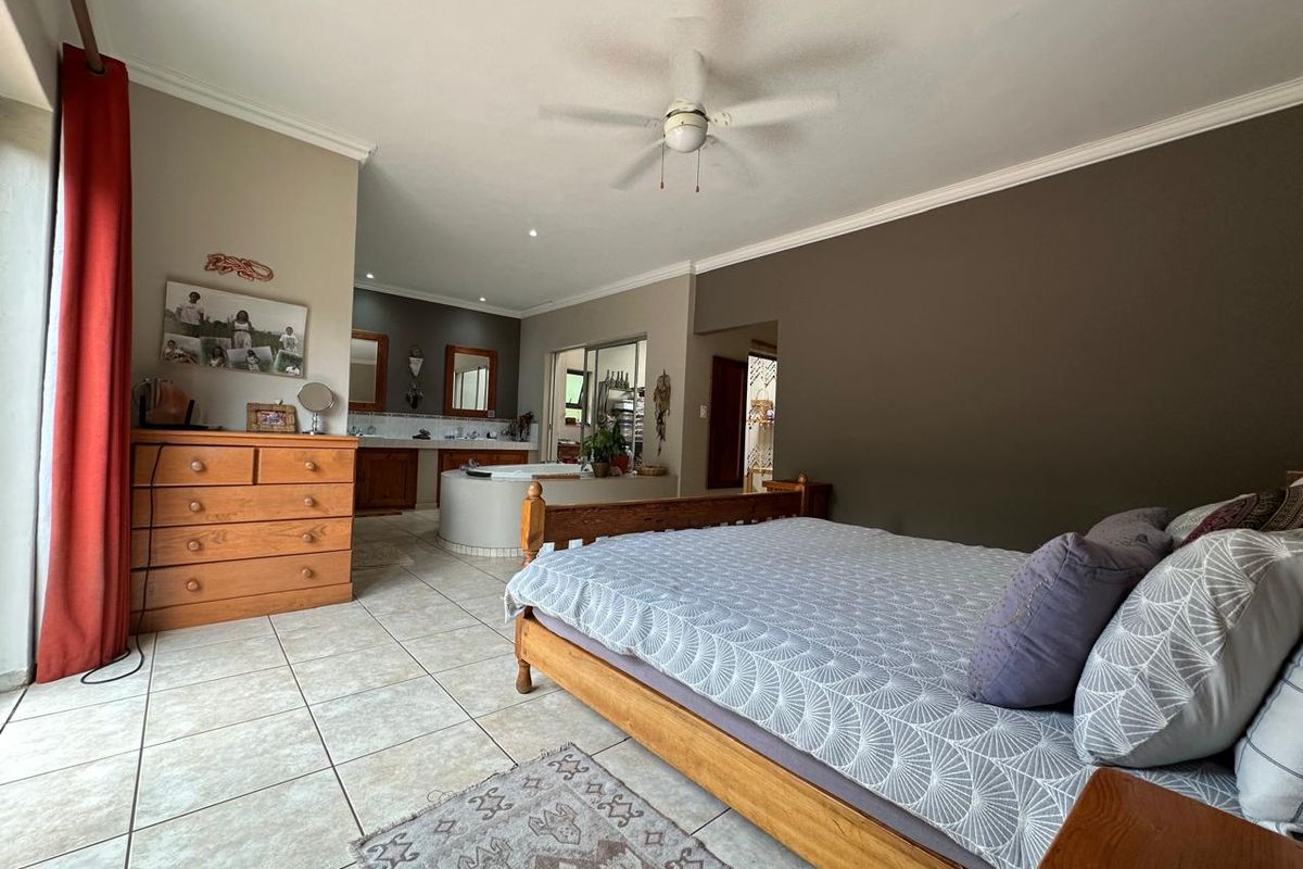 Spacious bedroom featuring tiled flooring, a ceiling fan, and an open-plan en-suite bathroom with a built-in bathtub and double vanity.