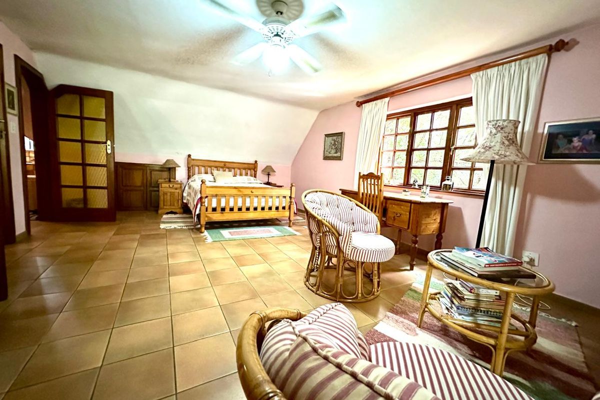 Spacious bedroom featuring tiled flooring, a ceiling fan, and large timber-framed windows, offering a comfortable and functional living space.