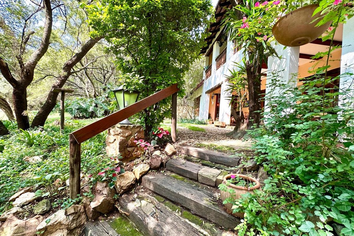 A rustic garden path featuring timber sleeper steps and stone retaining walls leading to the rear patio and balcony of the farmhouse.