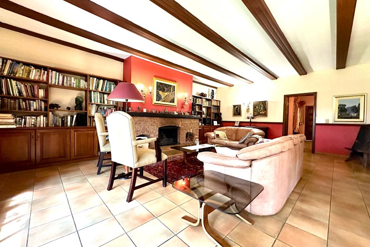 Spacious living room featuring exposed timber ceiling beams, a prominent stone-clad fireplace, and extensive built-in wooden cabinetry for storage.